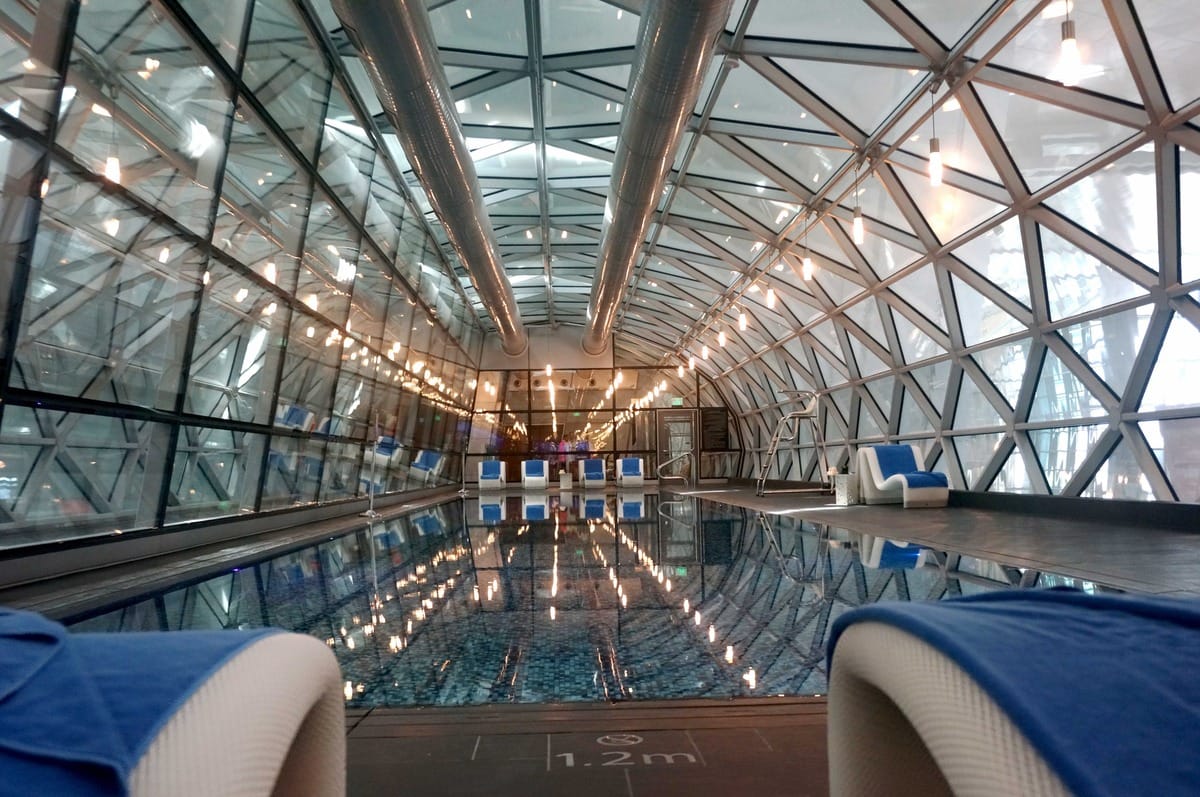Indoor 25-metre swimming pool with lounge chairs inside a glass-domed structure at Hamad International Airport in Doha, Qatar.